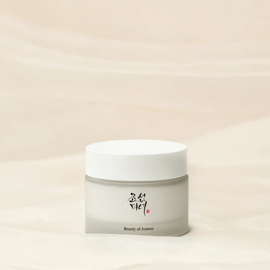 Flacon de la Dynasty Cream de Beauty of Joseon sur fond beige, mettant en avant son packaging élégant avec des motifs traditionnels. La crème est présentée dans un pot chic qui illustre son utilisation d'ingrédients naturels tels que le ginseng et l'huile d'olive, soulignant ses bienfaits hydratants et anti-âge.